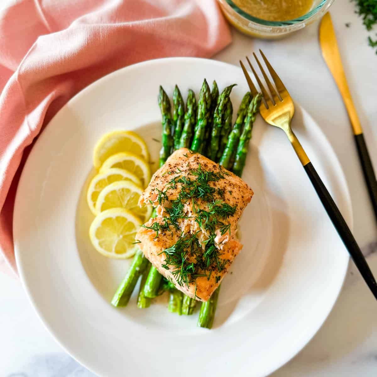 A white plate with air fried salmon filet with asparagus, lemon slices, and lemon brown butter sauce