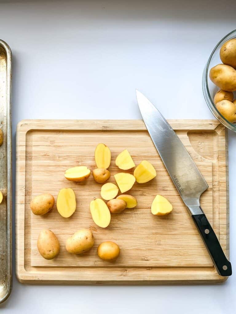 A cutting board with a chef's knife and baby potatoes being cut in half.