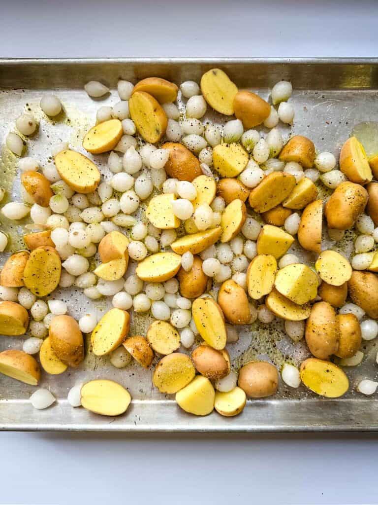A sheet pan with halved baby potatoes and pearl onions tossed with olive oil, salt and pepper.