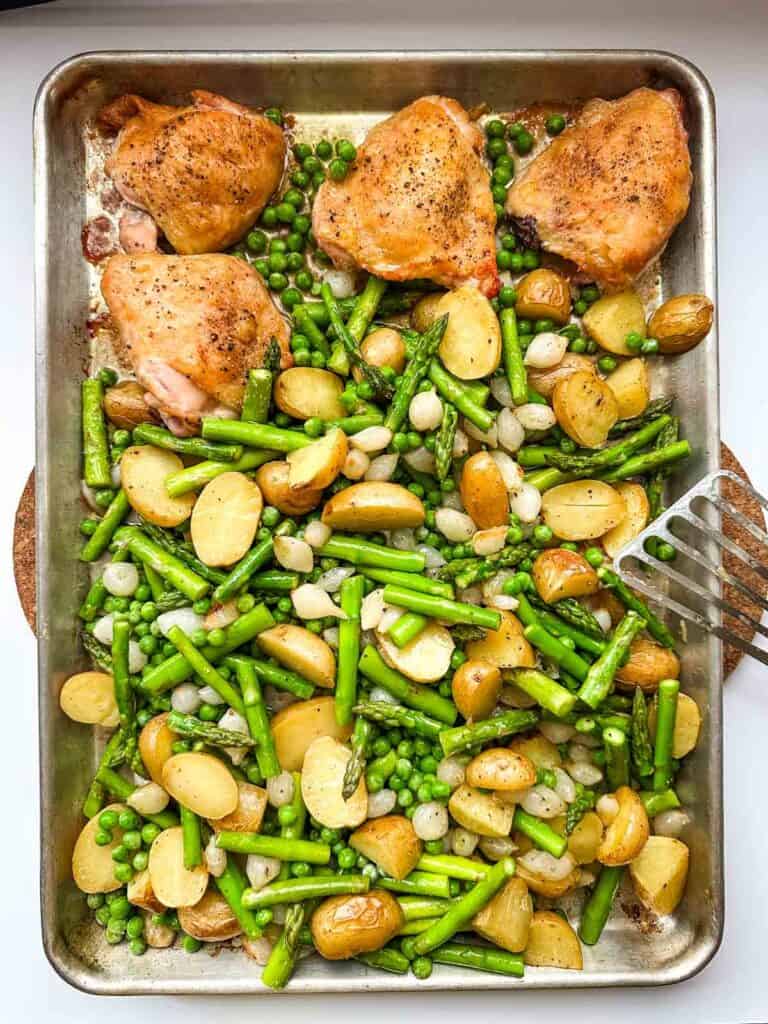 A sheet pan just out of the oven with roasted chicken, pearl onions, potatoes, asparagus and peas.