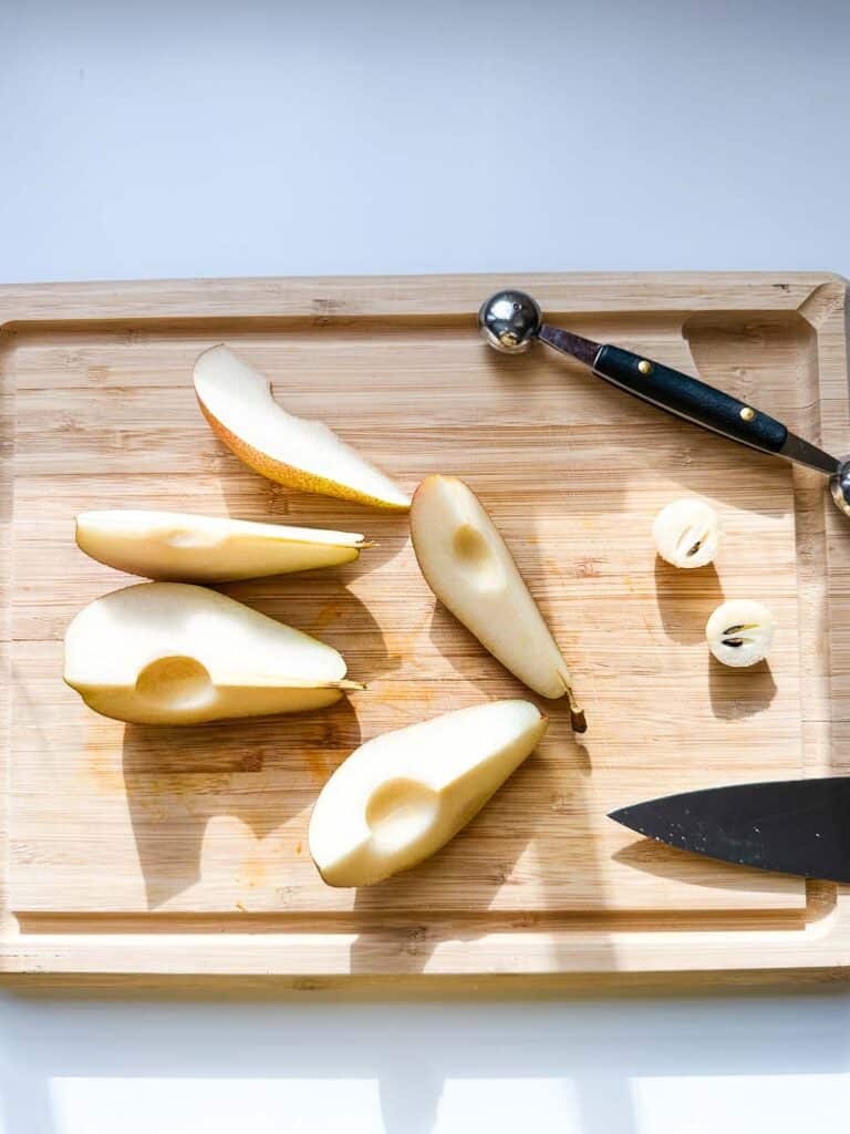 A cutting board showing a pear cut into wedges and cored with a mellon baller.