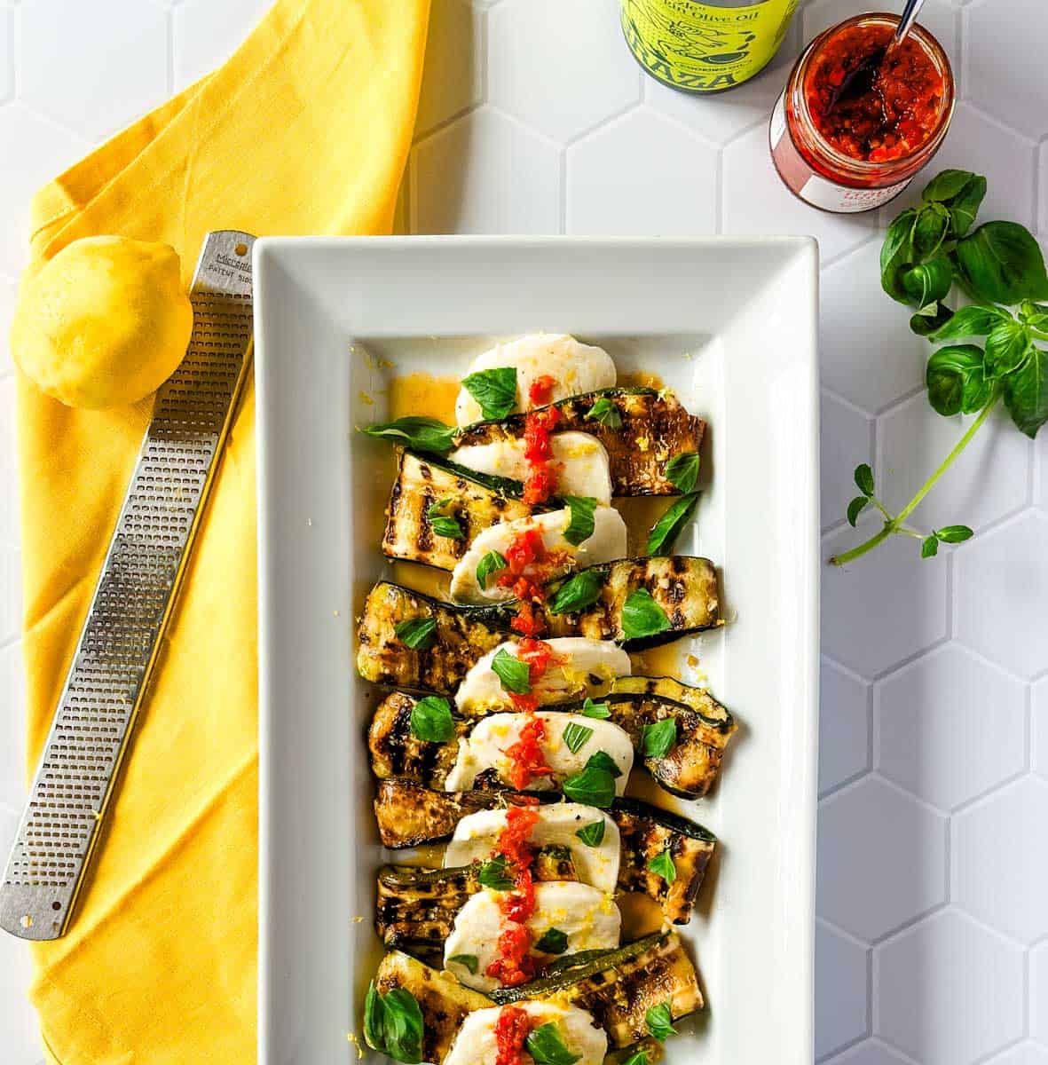 A white rectangular platter with grilled zucchini, mozzarella cheese, and calabrian chilies.