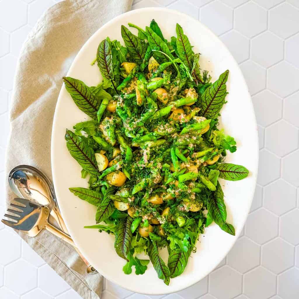 A large white oval platter with potato salad with asparagus and parmesan vinaigrette.