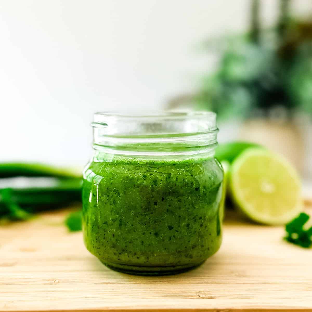 A small glass jar filled with green garlic basil vinaigrette on top of a cutting board.