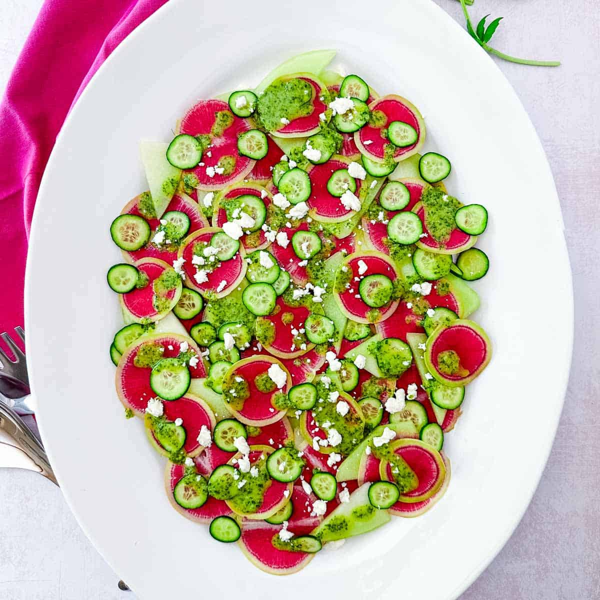 A large oval white platter with watermelon radish salad next to a hot pink napkin.