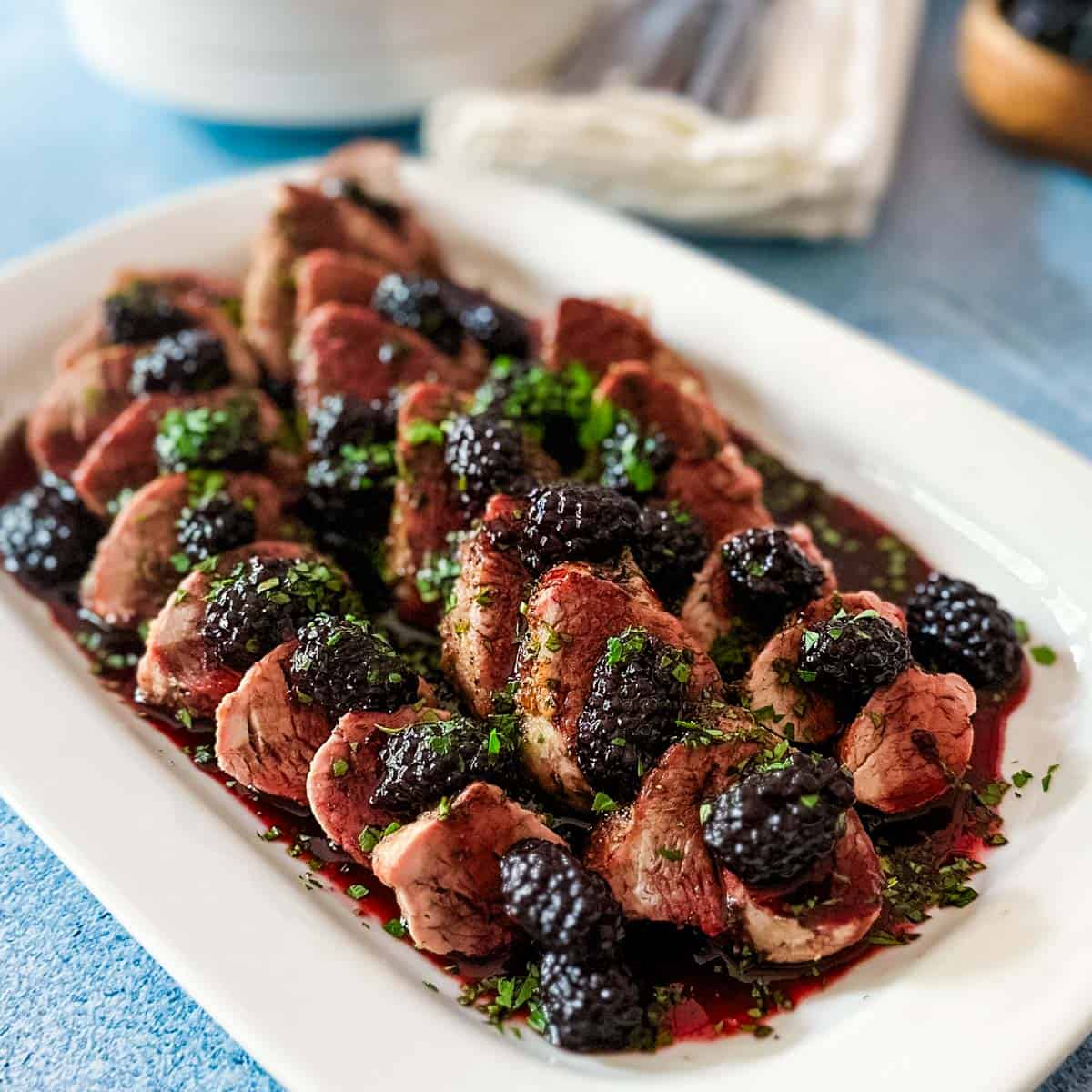 A white platter with sliced pork tenderloin covered in blackberry gastrique sauce.
