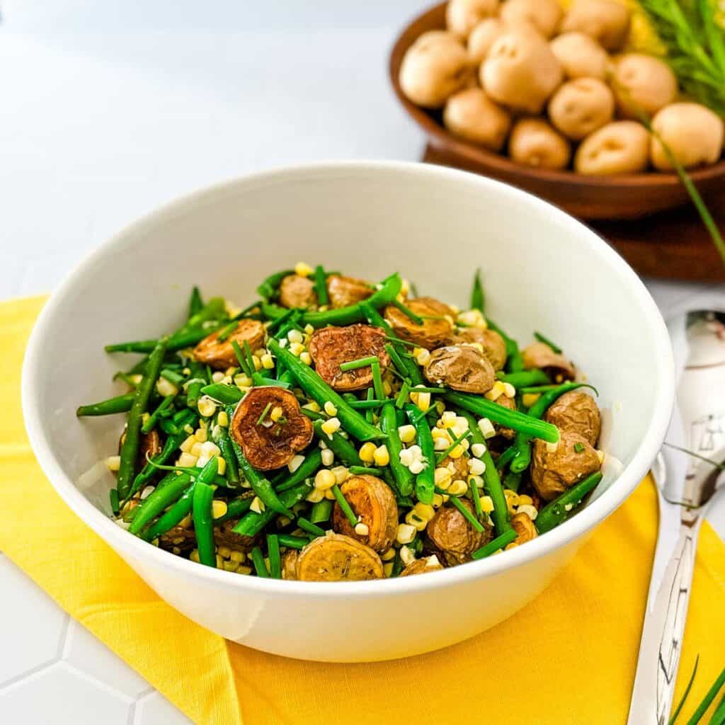 A white bowl on a yellow napkin filled with potato and green bean salad with corn vinaigrette.