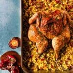 An overhead view of a whole roasted chicken on a bed of saffron rice on a blue background.