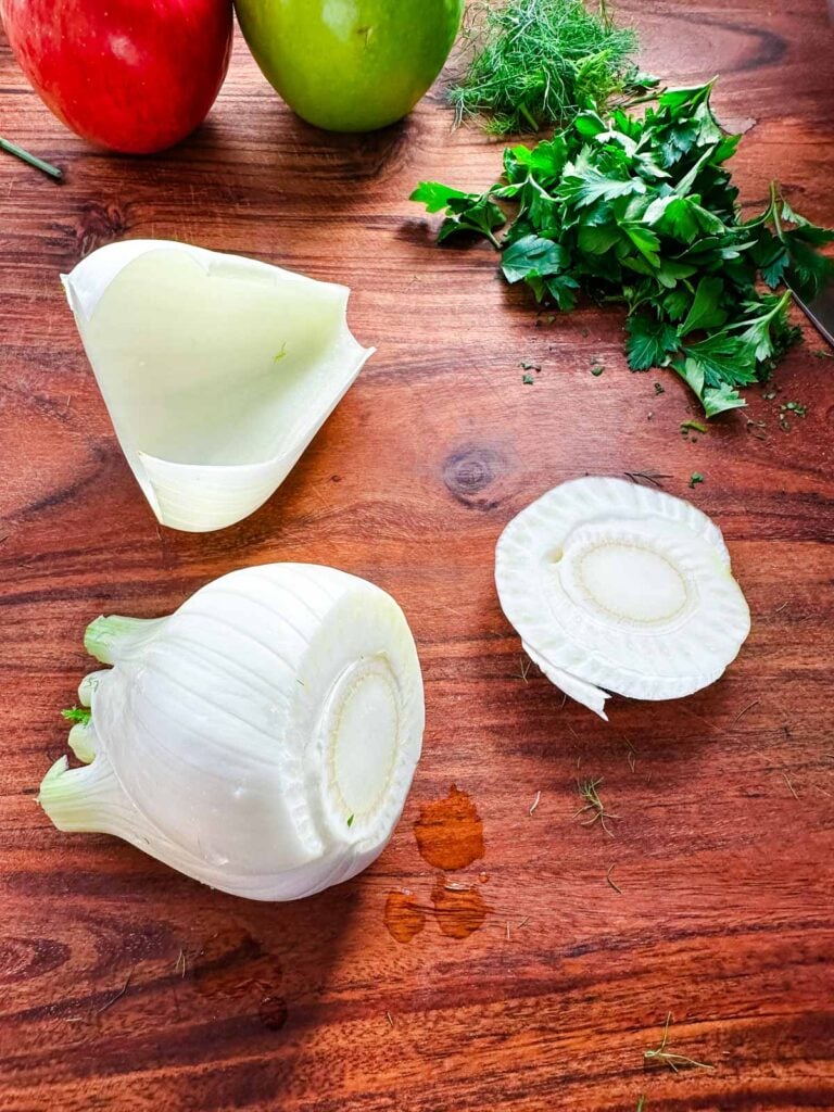 A fennel bulb on a cutting board with the bottom slice and outer leaves removed.