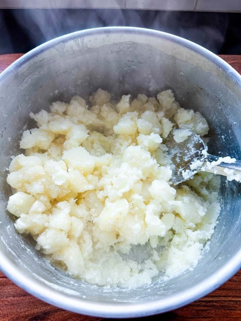Drained potatoes returned to the pot on the stove over medium-low heat to dry them out.