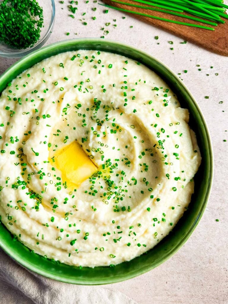 A large bowl of boursin mashed potatoes next to a bunch of chives and small bowl of chopped chives.