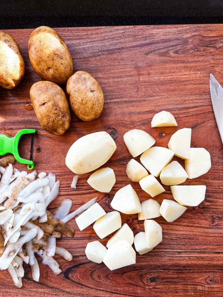 A pile of russet potatoes peeled and chopped on a cutting board.