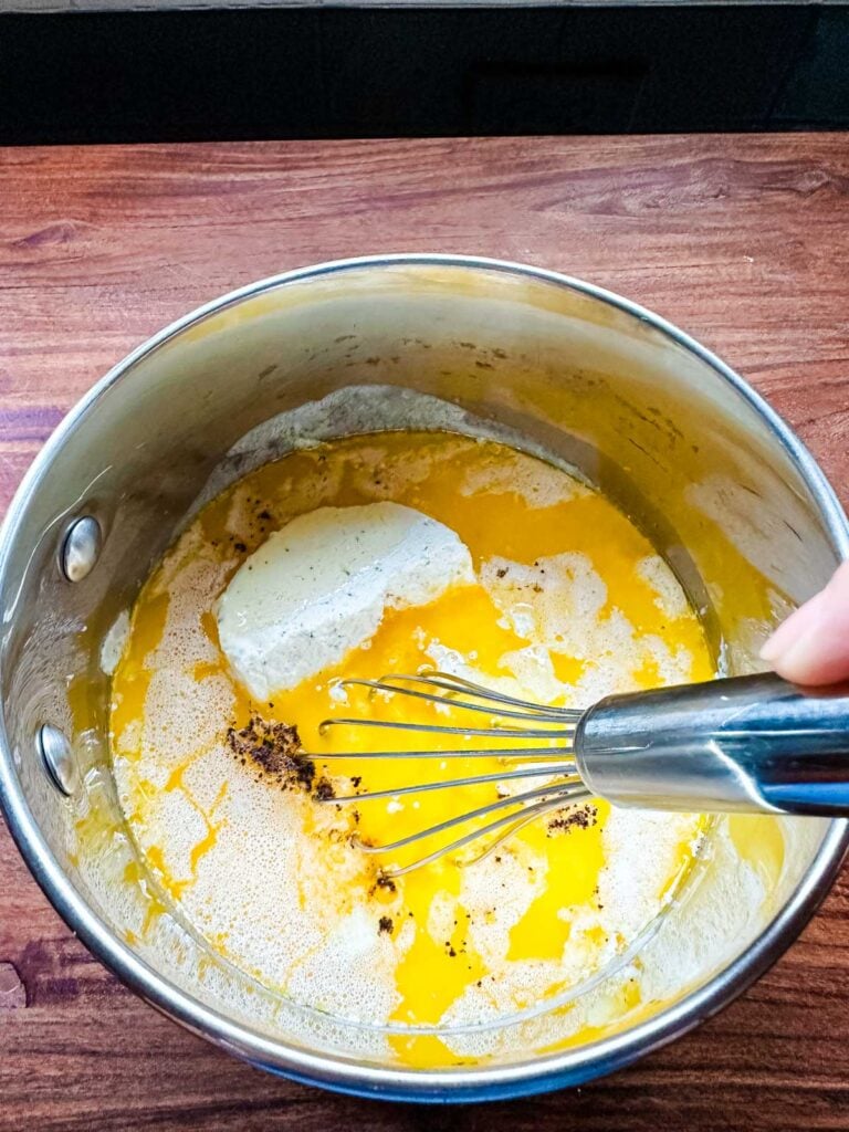 Boursin cheese being whisked into a saucepan with cream and butter.
