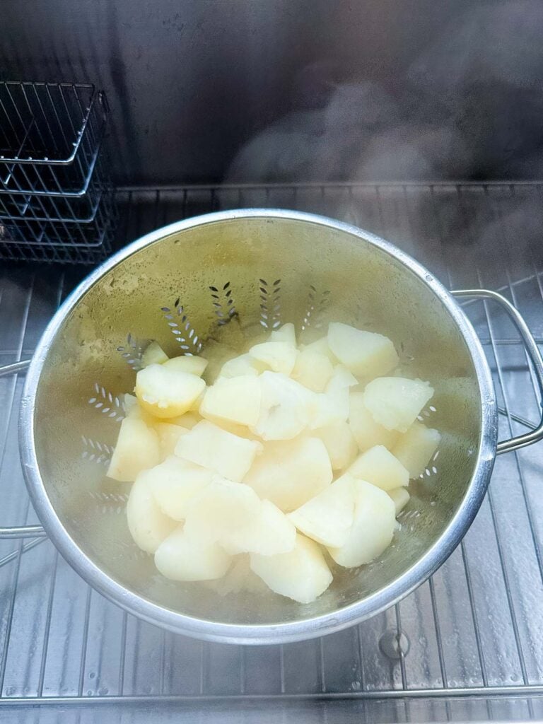 Cooked potatoes being drained in a colander in the sink.