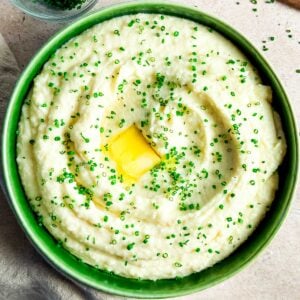 A large bowl of boursin mashed potatoes next to a bunch of chives and small bowl of chopped chives.