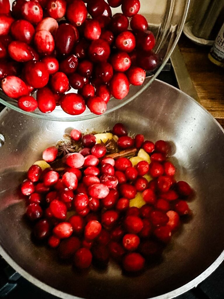 Cranberries being added to spices cooking in a saucepan.