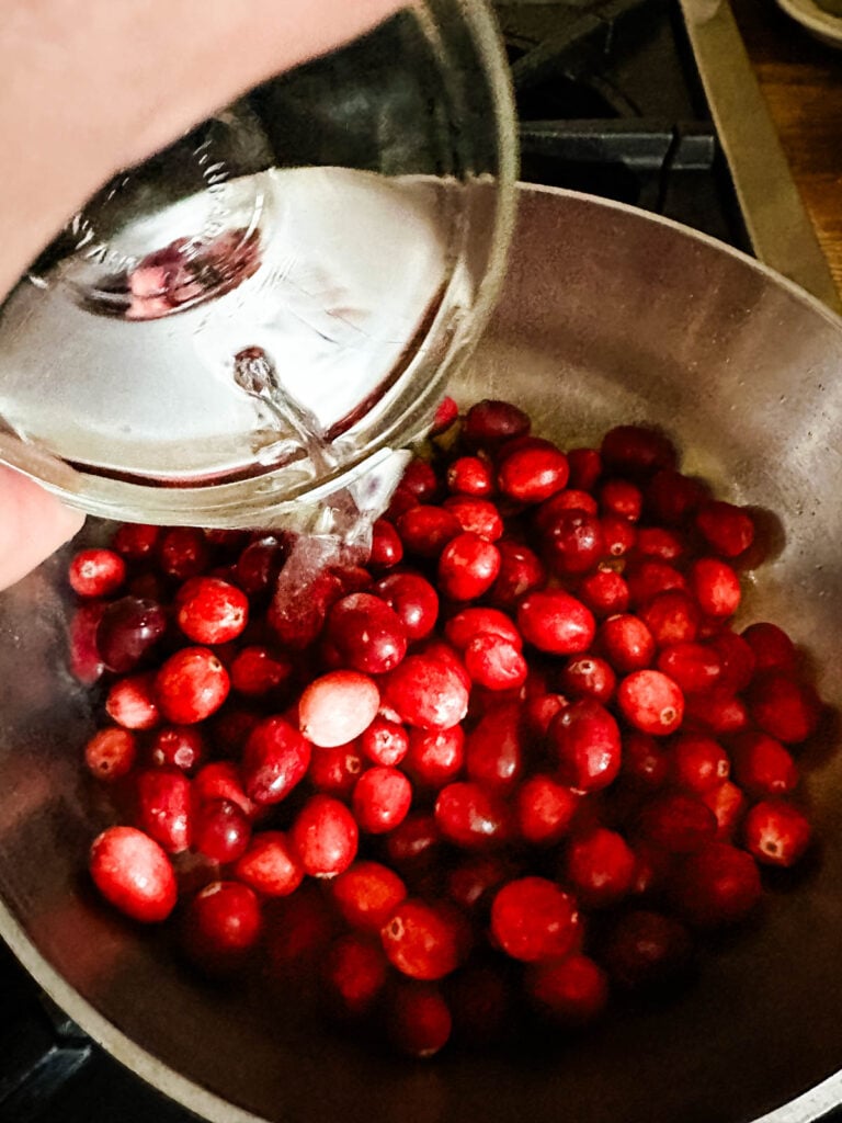 Water being added to cranberries cooking in a saucepan.