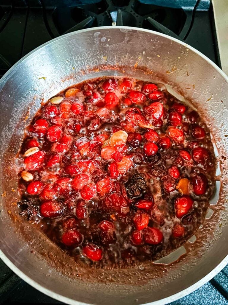 Spiced cranberry sauce cooking in a saucepan on the stove.