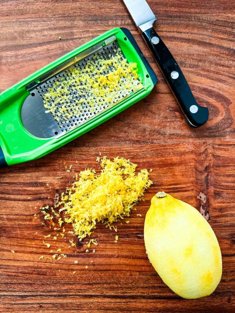 A lemon next to a pile of lemon zest and a microplane zester on a cutting board.