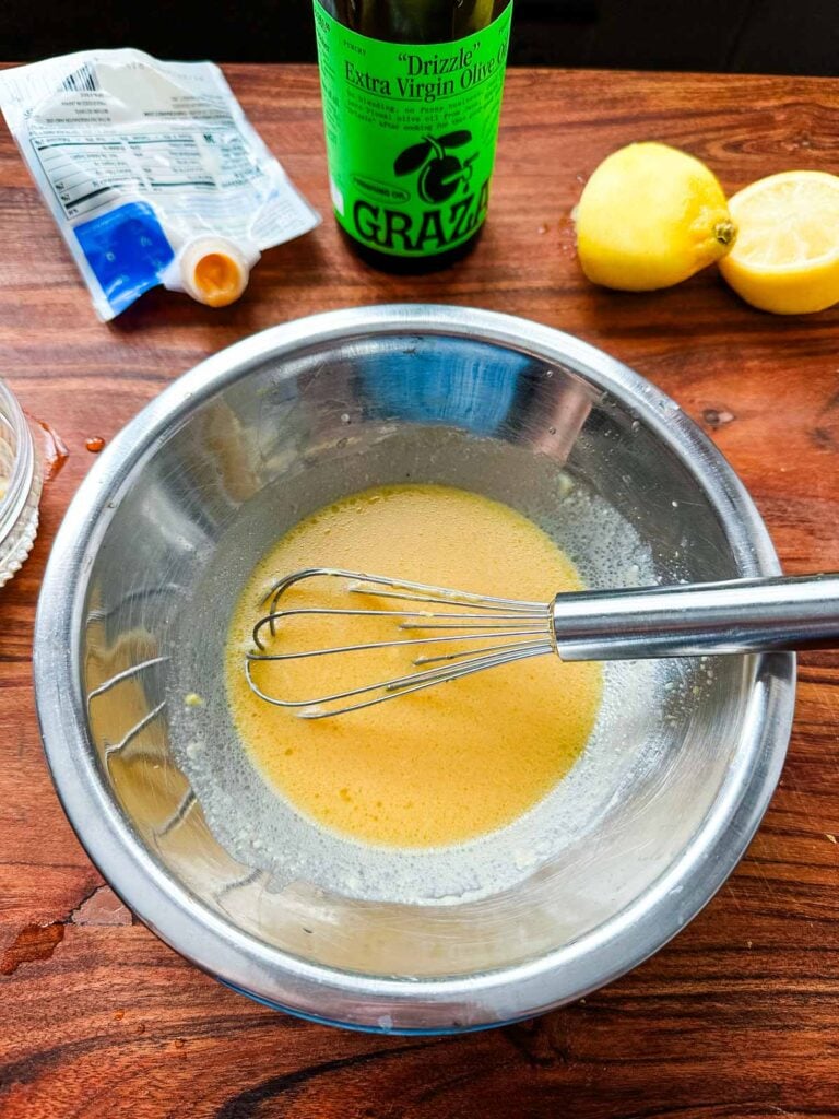 A small stainless steel bowl of miso glaze with a whisk ready to be added to roasted brussels sprouts.