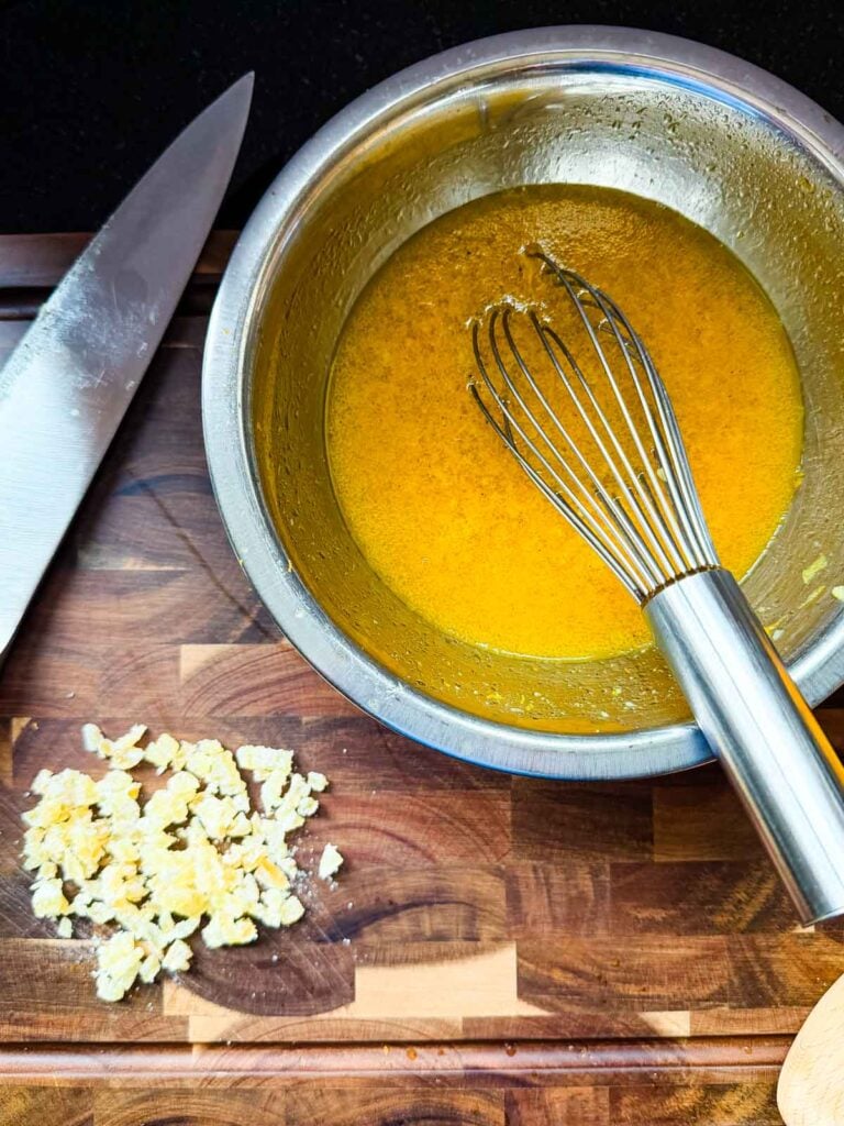 A bowl of ginger vinaigrette next to a pile of chopped crystallized ginger.