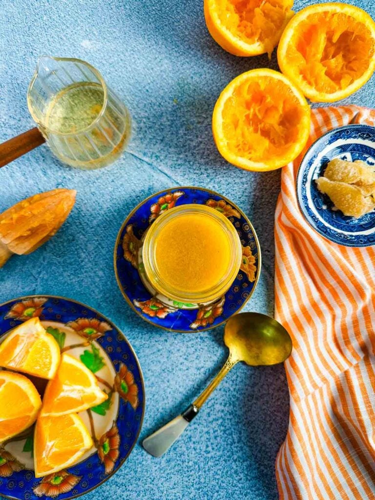 An overhead view of a jar of vinaigrette, a plate of oranges, and an orange and white striped napkin on a blue background.