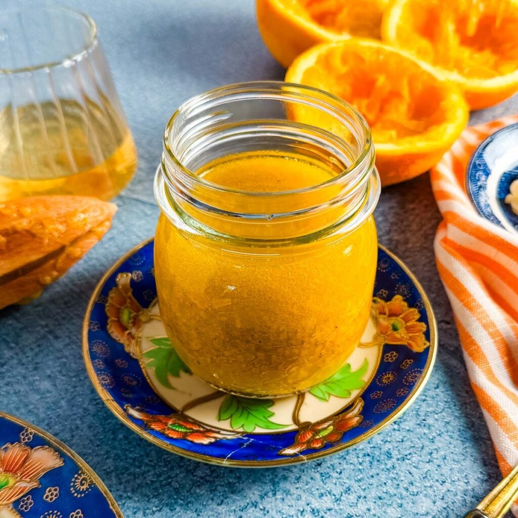 A glass jar of ginger vinaigrette on a small blue and orange china plate.